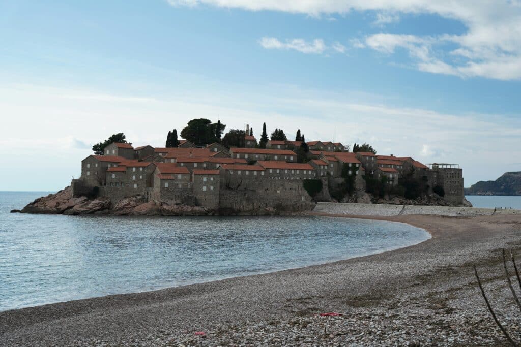 Stone coastal village on a rocky island with red-tiled roofs, set against a calm sea and clear sky
